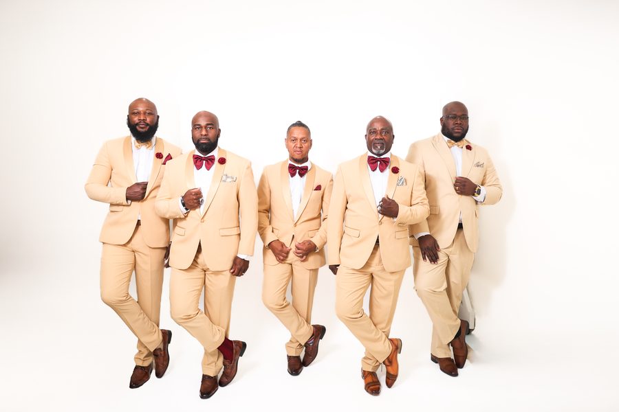 The five members of the group in matching cream suits on white